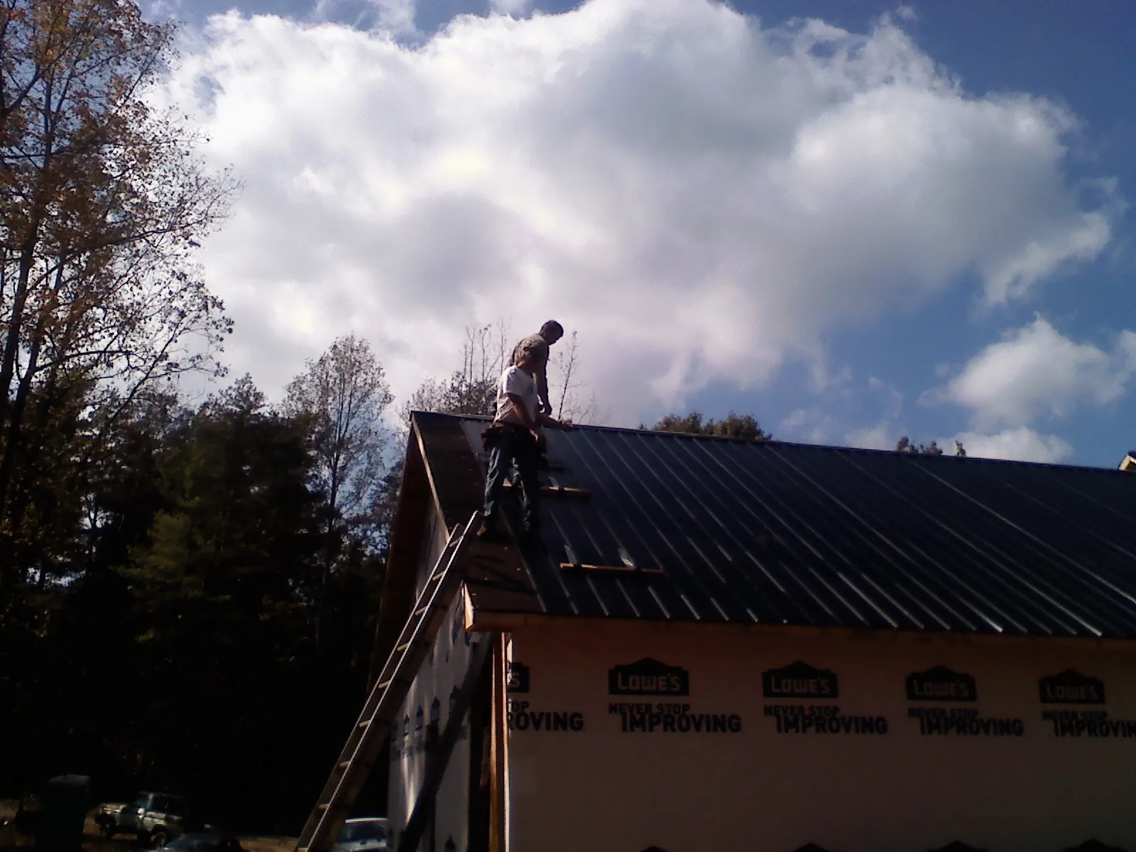 Roofer fastening dark metal panels high against a cloudy sky, from a Roof Inspection job in Colton